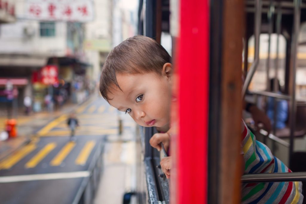 A child peering out the window of a moving tram in Hong Kong, capturing urban exploration.